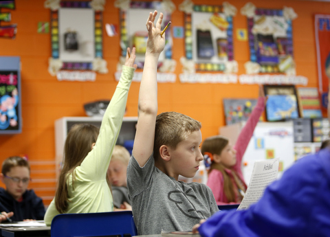 This is a picture of elementary students raising their hands in a classroom.