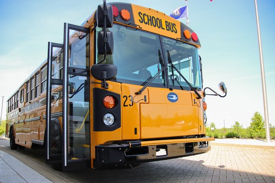 Photo of a school bus with doors open in front of a flag pole.