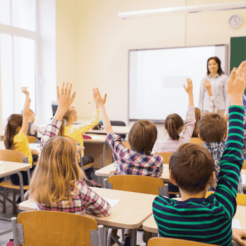 Photo of students raising their hands in a classoon.