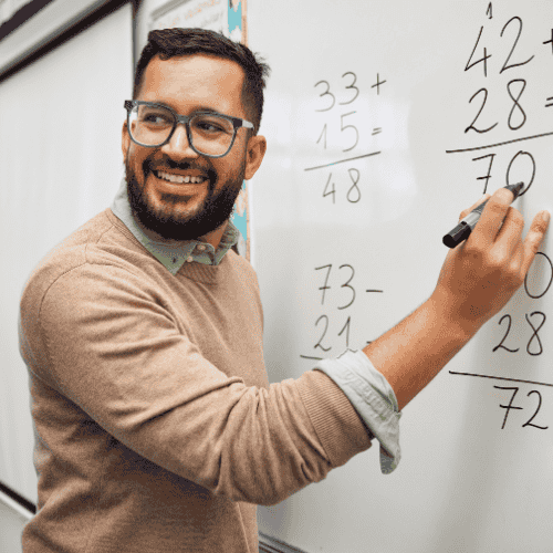 Photo of male teacher writing math problems on a white board.