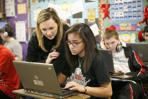 A teacher helps a student on a computer.