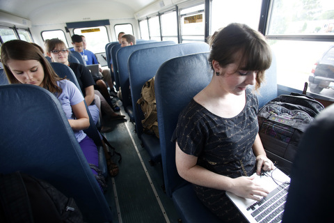 Students work on laptop computers while riding a schoolbus.